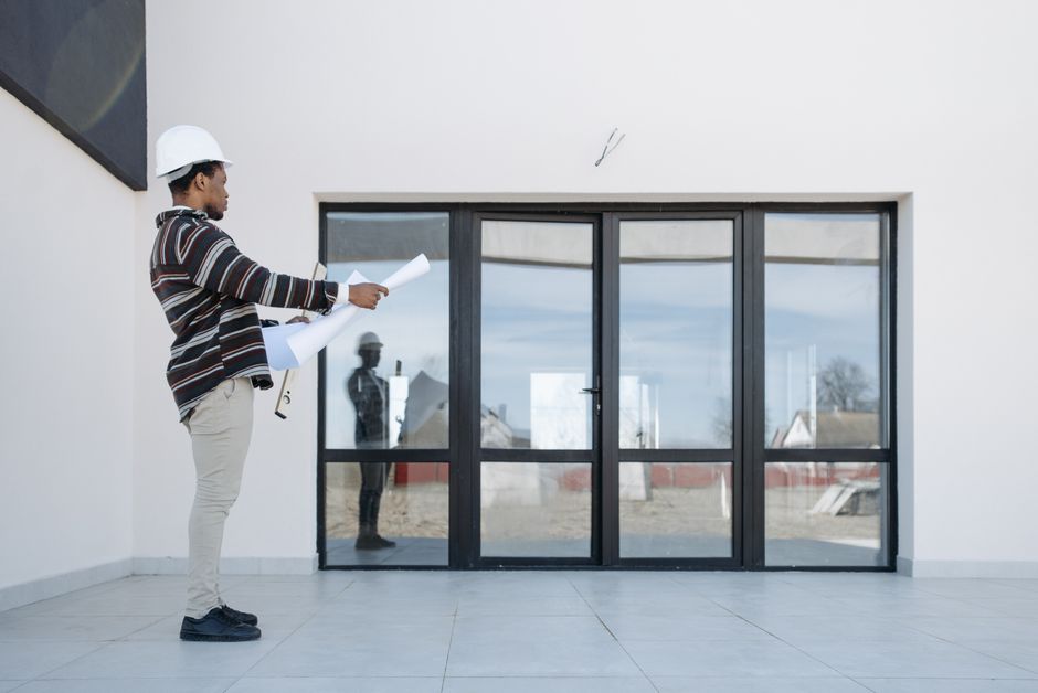 Architect wearing hard hat holding plans in front of modern glass doors.