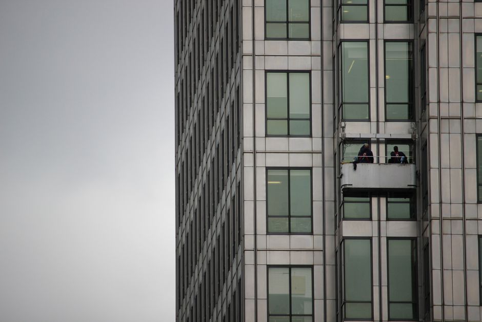 Window cleaners working on a platform on a modern high-rise building on a cloudy day.